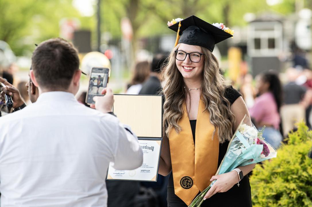 Graduated student poses with flowers and degree holder.